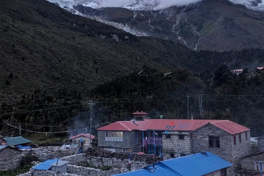 Traditional stone teahouse with red roof against backdrop of Himalayan mountains and glacier